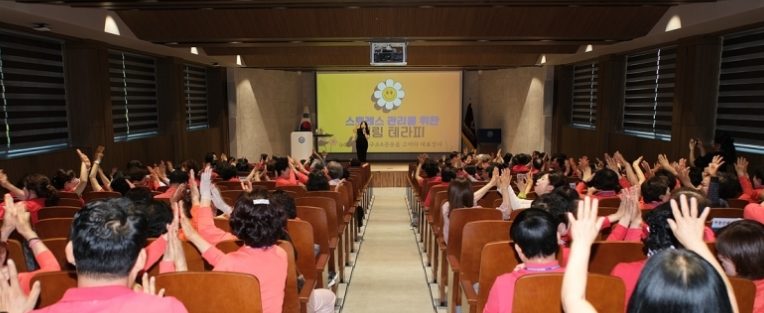 단체복을 입은 기관 직원들이 박수 치며 참여하는 스트레스 관리 웃음 테라피
