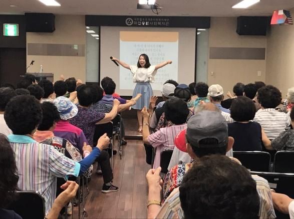 어르신들과 함께 두 팔을 들고 웃음 체조를 하는 고아라 강사