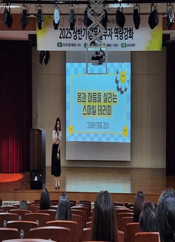 학교 강당 무대에서 학부모와 학생 대상 웃음 특강을 진행하는 고아라 강사