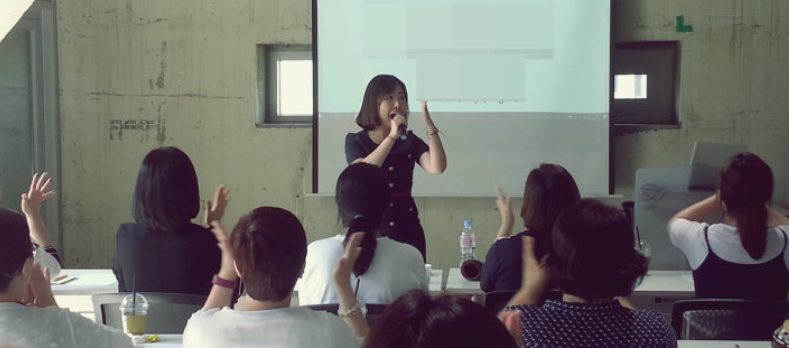 워크숍에서 참가자들이 손을 들고 웃으며 참여하는 고아라 강사의 웃음 테라피